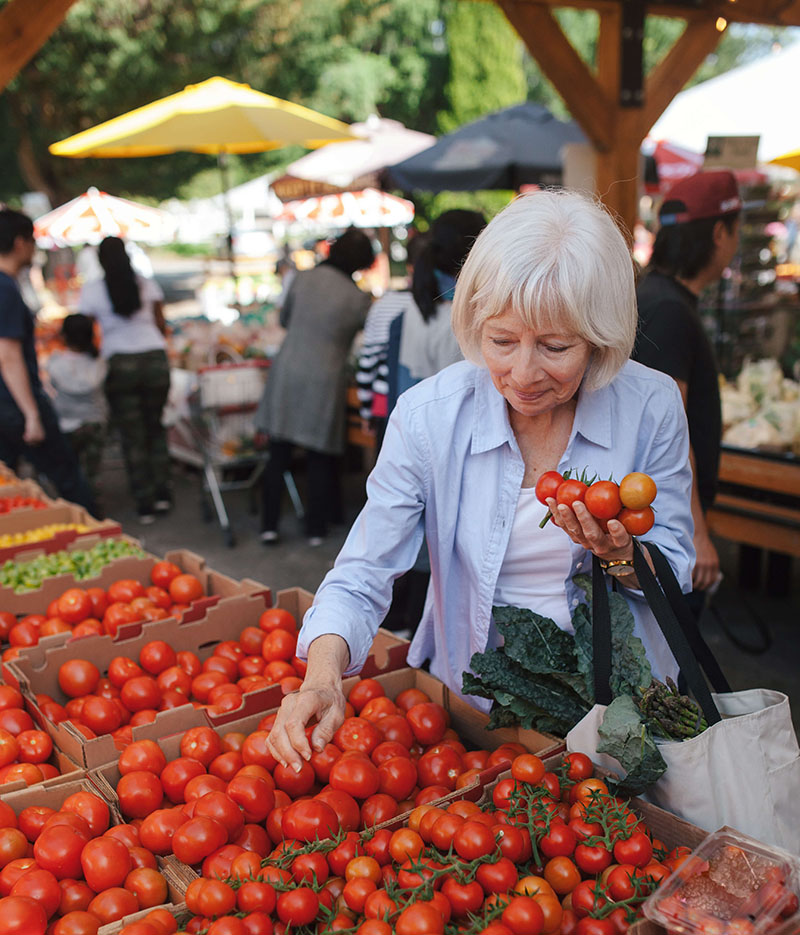 A woman selecting ripe tomatoes at a bustling farmers market