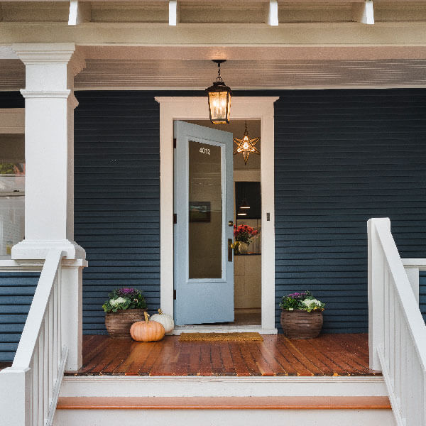 A light blue door is left open to invite guests inside from the front porch of a single-family home with deep blue siding