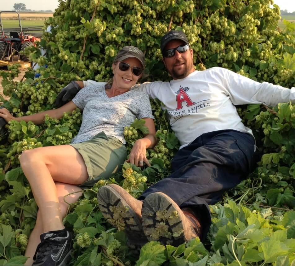 Ron & Michelle Yovich, the majority owners of Mountain Cowboy Brewing Company, taking a photo sitting on top of a pile of freshly-harvested hops
