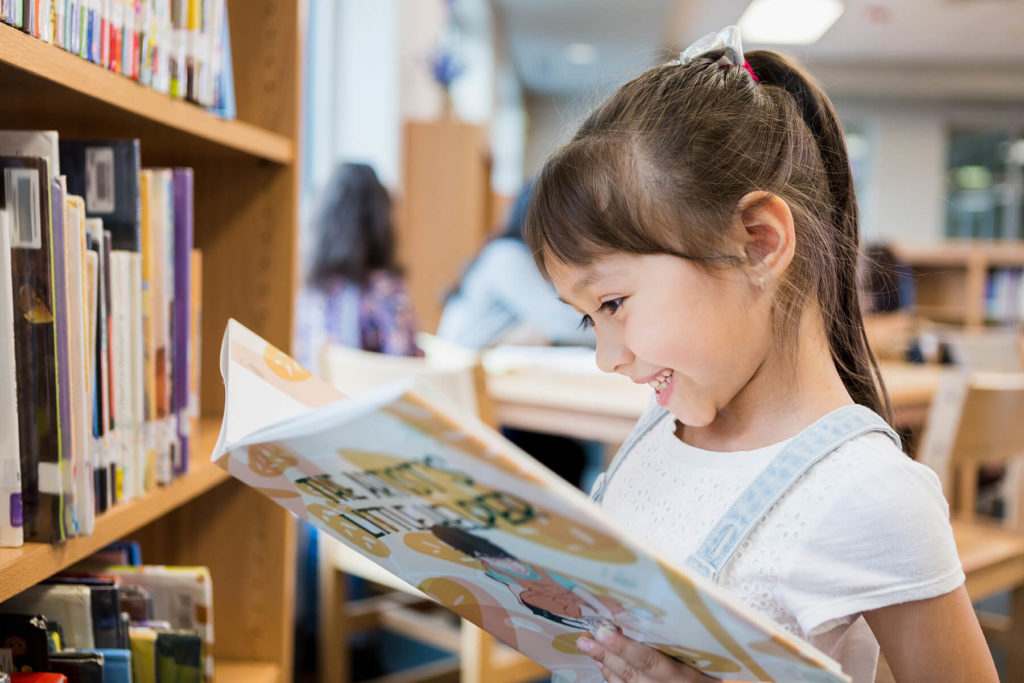 A little girl reading a book in a library.