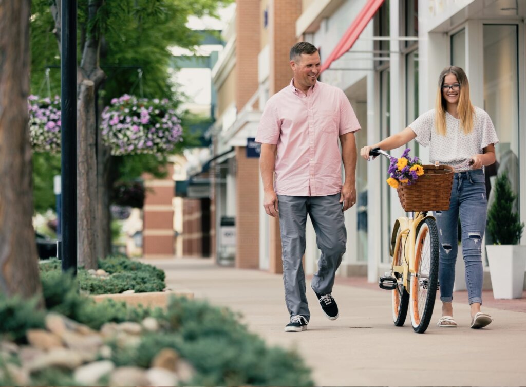 A man and woman walking down a sidewalk with a bicycle.