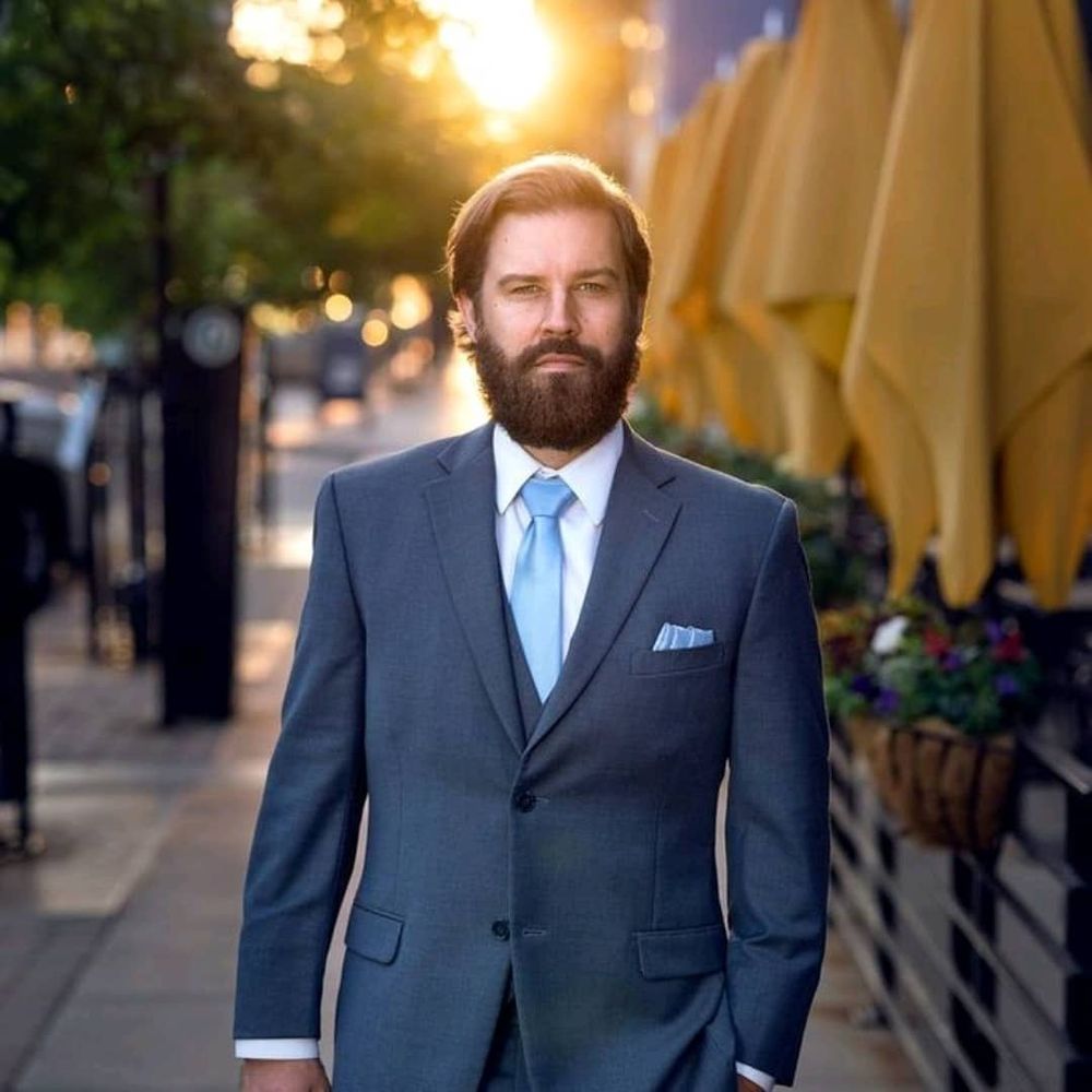 Image of man wearing a grey suit and blue tie