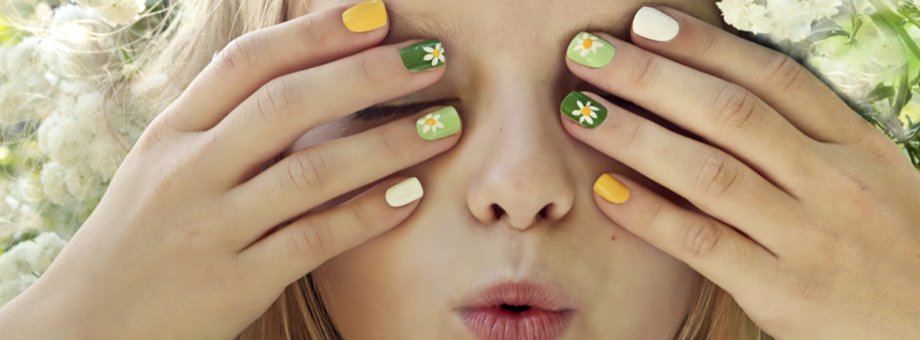 Image of young girl with green, yellow, and white painted nails holding hands over her face