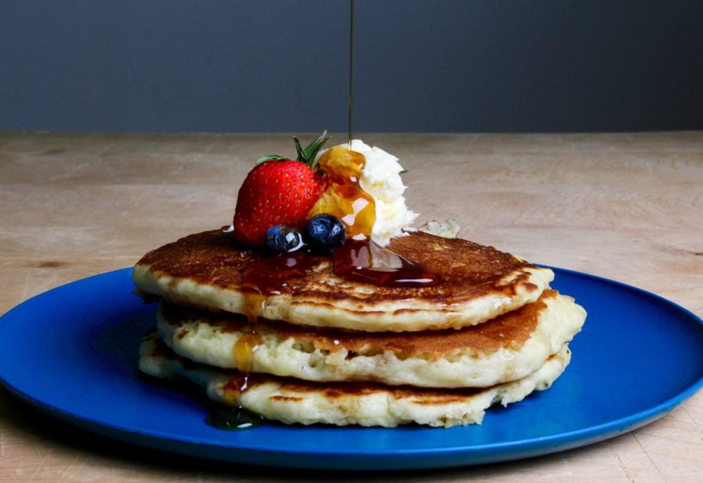 Image of a stack of pancakes with berries, butter, and syrup on top
