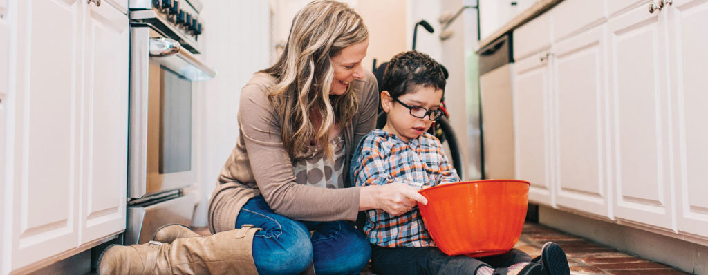Image of happy mom sitting on floor with young son holding an orange bowl