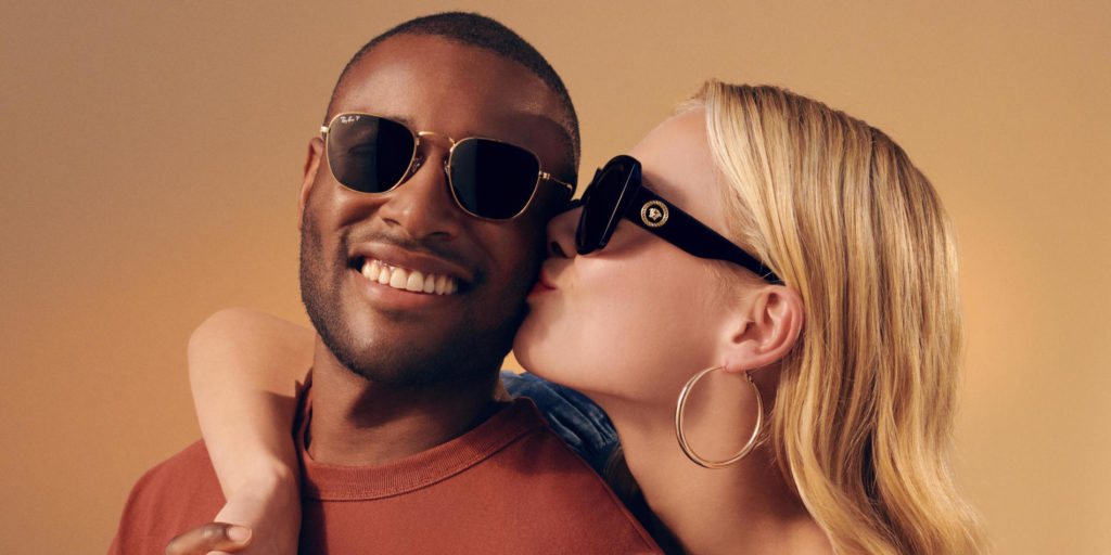 Image of woman wearing sunglasses kissing the cheek of a man wearing sunglasses