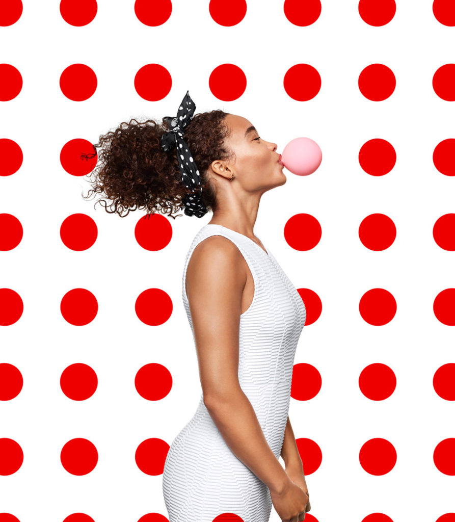 Image of a woman blowing a bubble gum bubble with red polka dots in the background