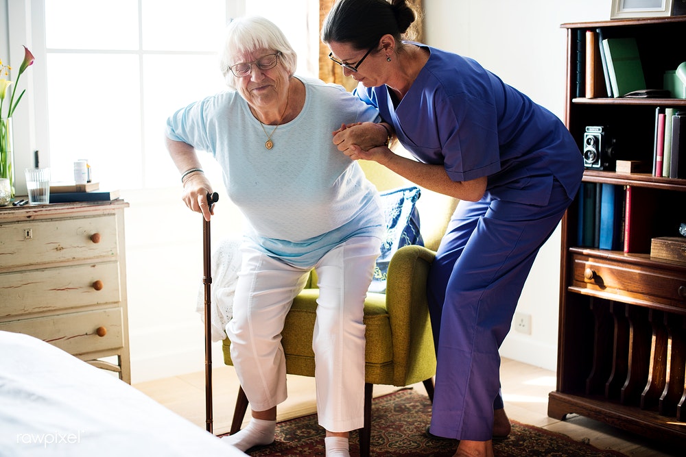 Image of caretaker helping a senior woman get out of a chair