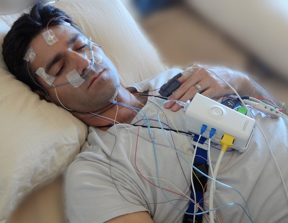 Image of man doing a sleep analysis with wires taped to his head and face