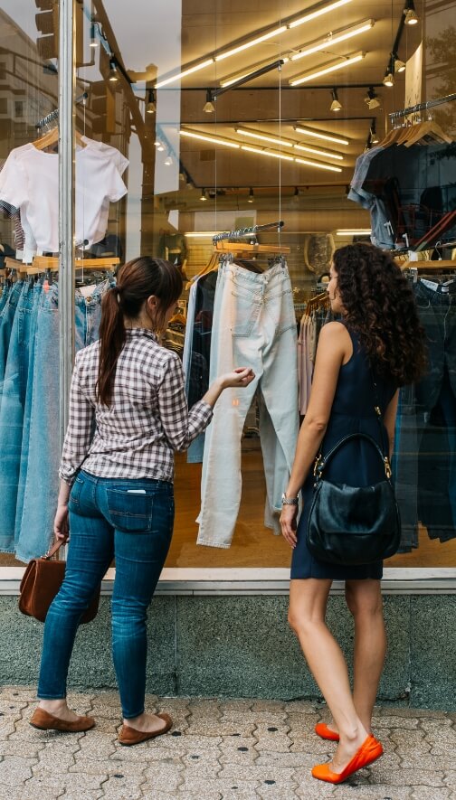 Image of two women looking at a pair of jeans through a storefront window