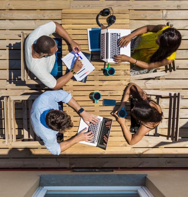 Image of group working outside on computers at a table while drinking coffee
