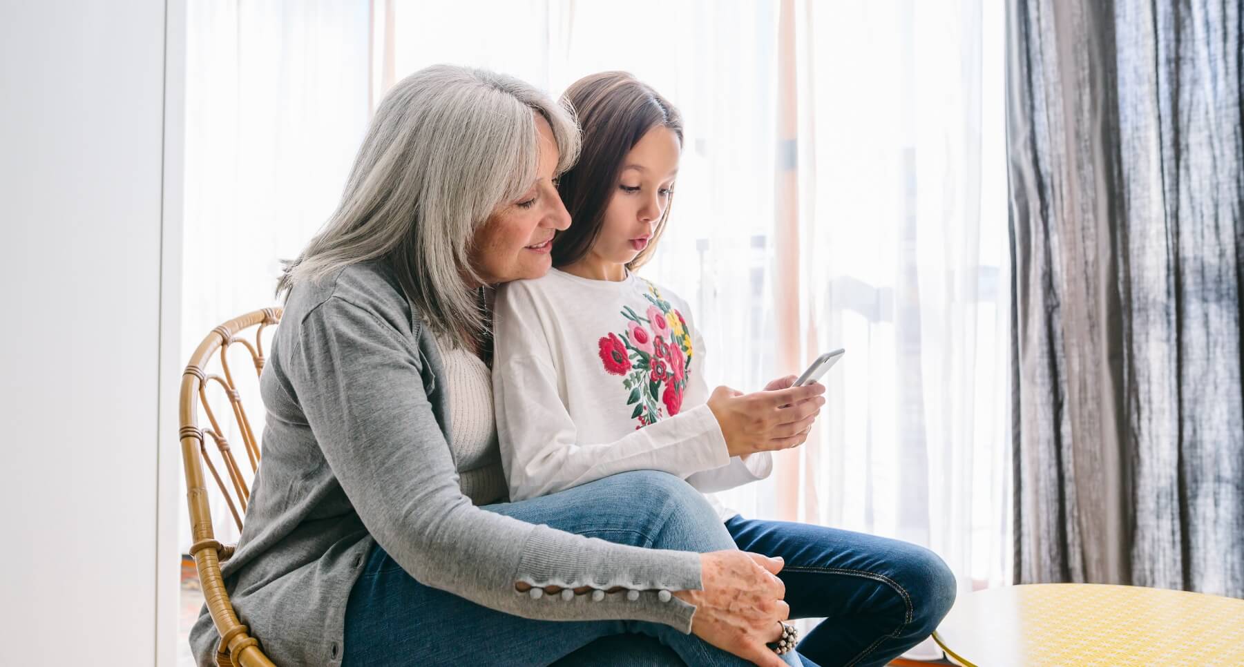 A woman and a girl sitting in a chair looking at a cell phone while dining together.