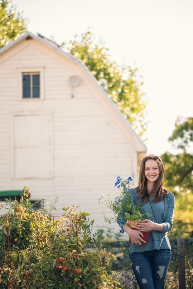 A young woman standing in front of a white barn, holding a bouquet of flowers, showcasing New Homes in Loveland.