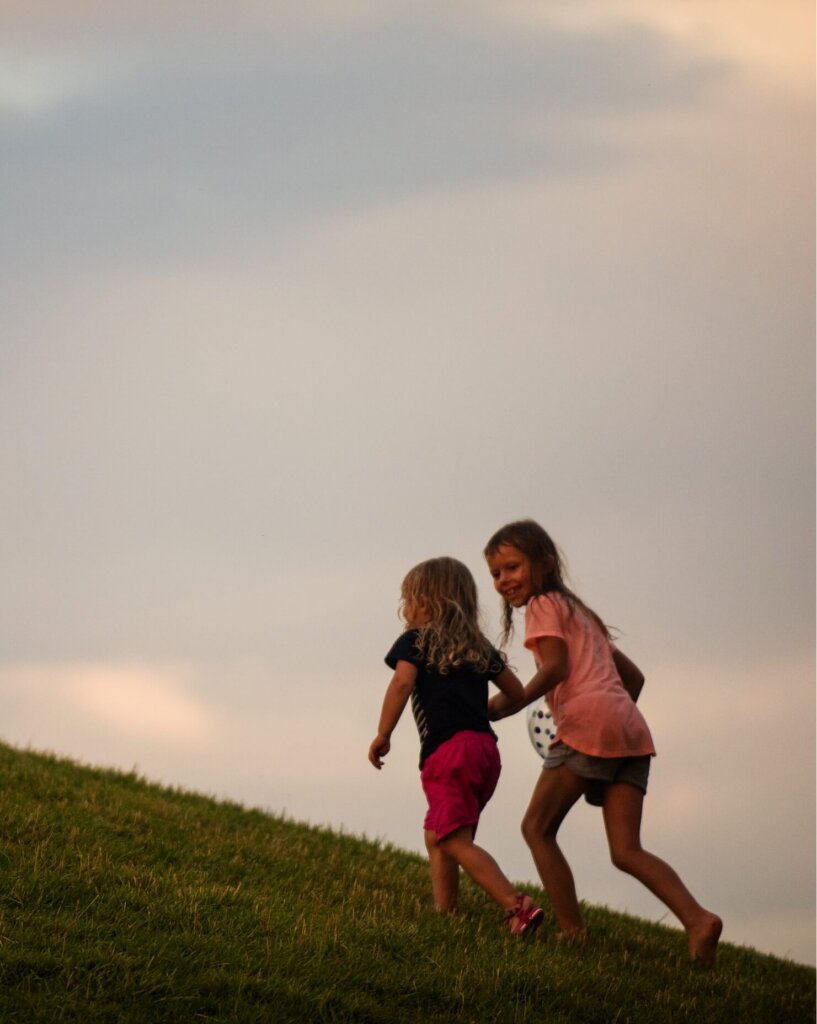 Two girls running on a Certified Wild grassy hill at sunset.