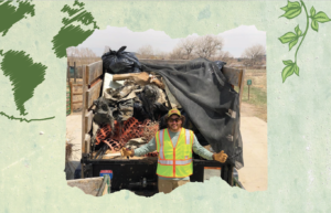 A person wearing a high-visibility vest and gloves stands in front of a trailer full of collected trash with a smile, under an overcast sky in Loveland, Colorado.