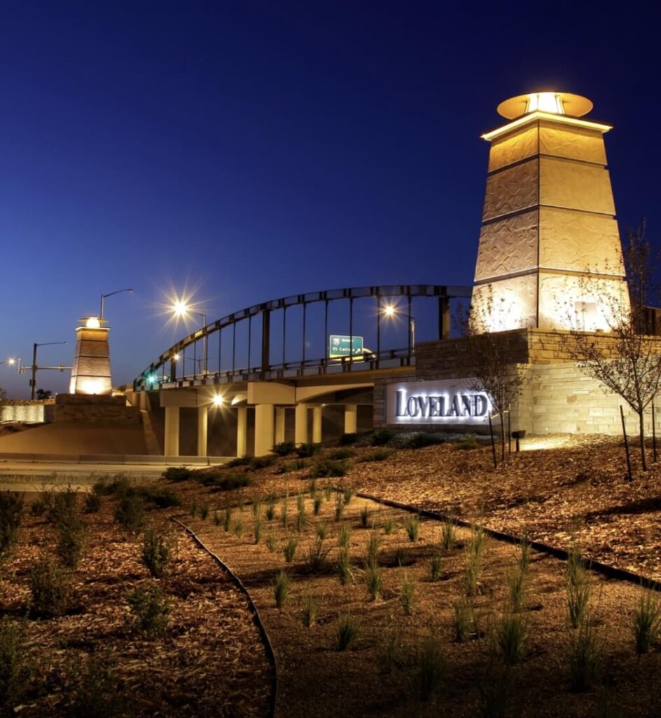 A well-lit bridge at night in Loveland, Colorado, with illuminated pillars on either side and a sign reading "Loveland" in the foreground—the perfect gateway to new homes in Centerra.
