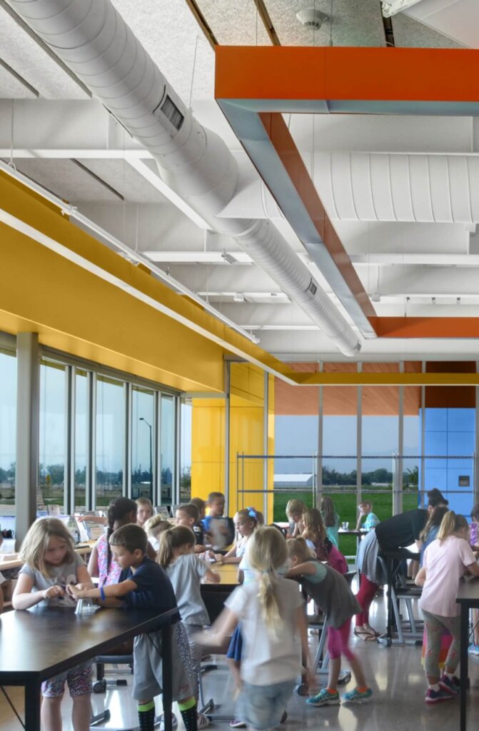 A group of children are engaged in activities at tables in a brightly lit and colorful classroom with large windows, located within the vibrant community near Centerra in Loveland, Colorado.