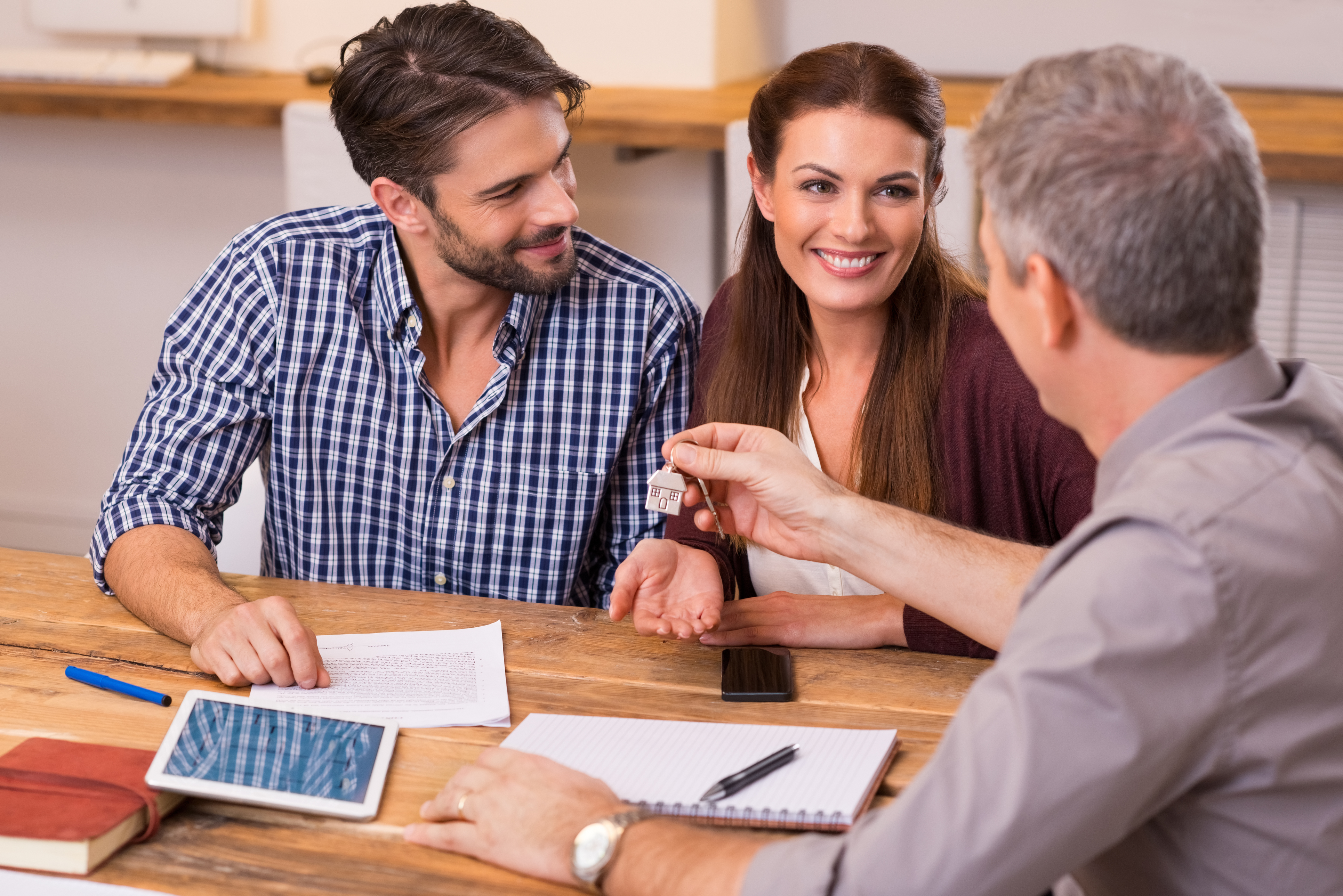 Young happy couple receiving house keys from real estate agent. Giving keys of new house to young couple. Smiling couple signing financial contract for mortgage.