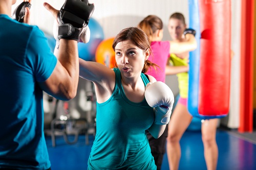 Woman Boxer hitting the sandbag, her trainer is assisting