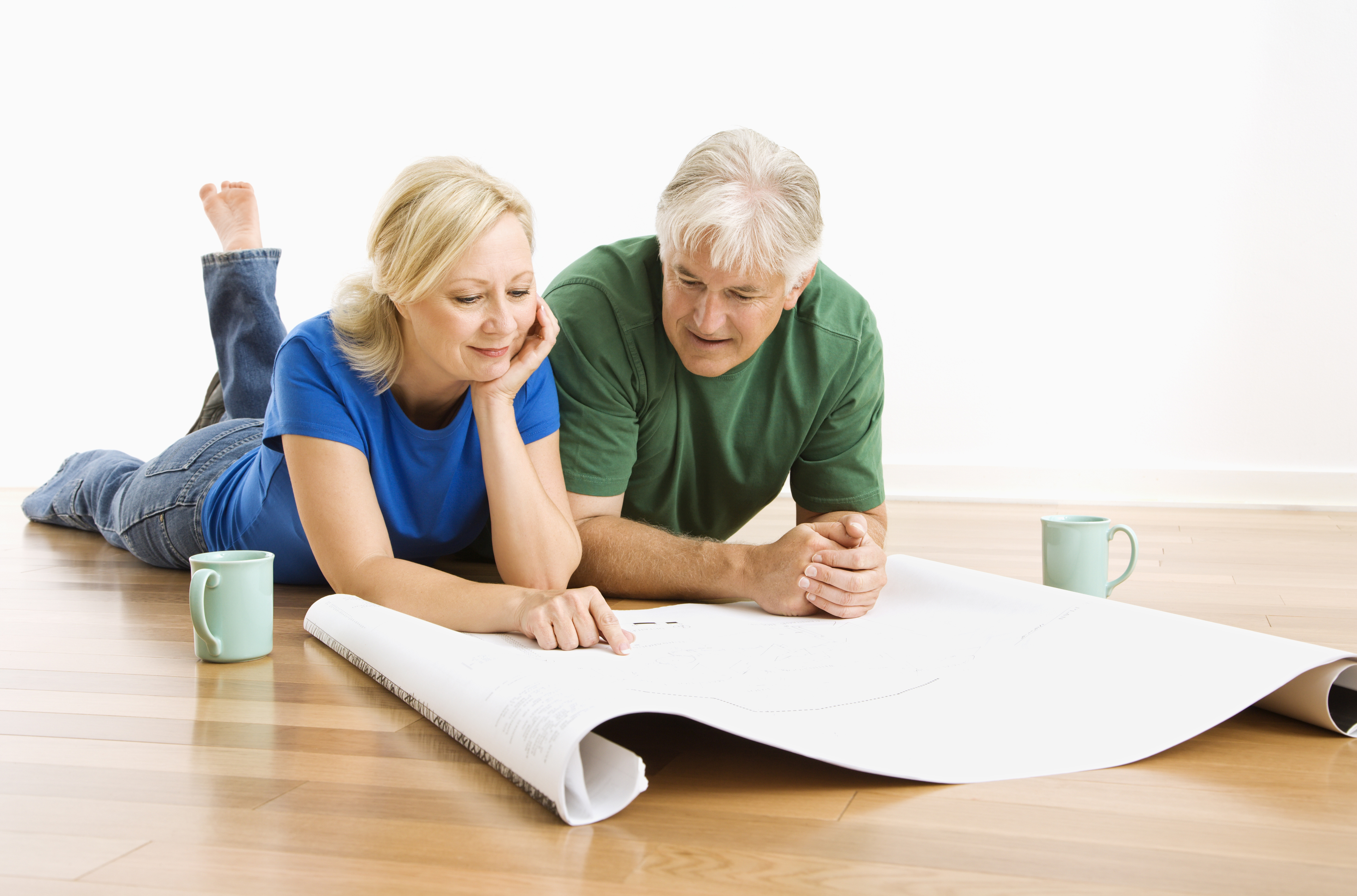 Middle-aged couple lying on floor looking at architectural blueprints together.